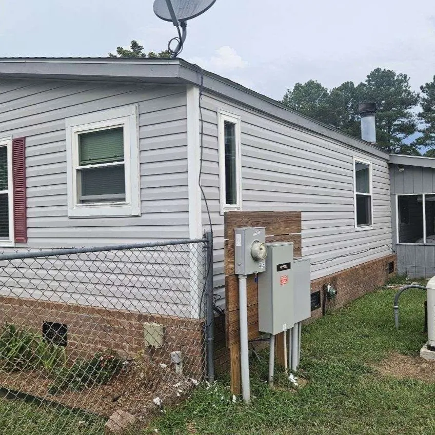 A light gray house with red shutters and a satellite dish, featuring an electrical panel and a generator.